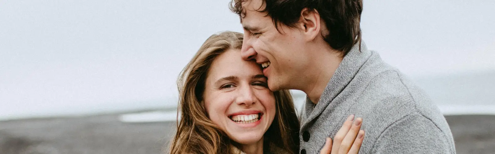 glueckliches-paar-am-strand-liebesbeziehung Ein verliebtes Paar lacht und umarmt sich am Strand â Symbol fĂŒr eine erfolgreiche Online-Partnersuche.