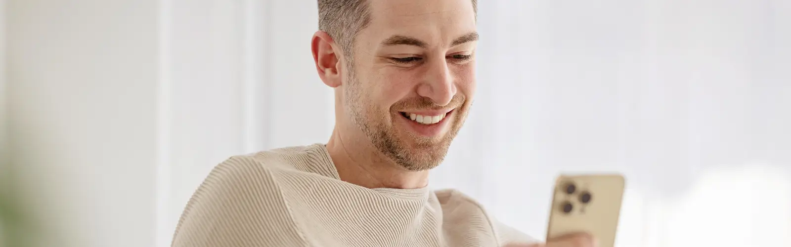 mann-smartphone-online-dating-app-laecheln Ein Mann sitzt entspannt auf dem Sofa und lÀchelt beim Lesen einer Nachricht in einer Dating-App auf seinem Smartphone.
