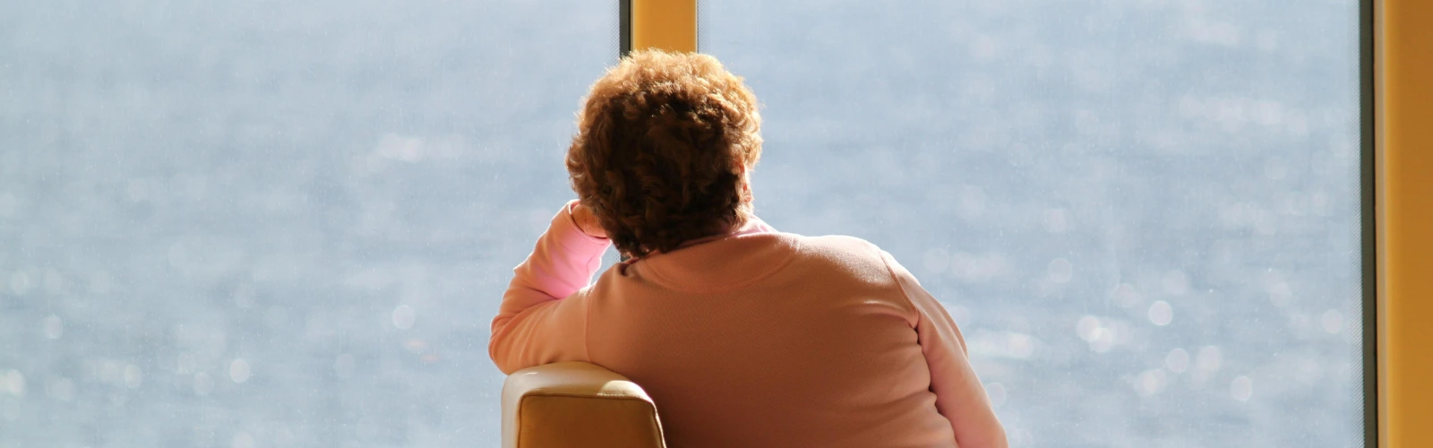 viele-dates-aber-keine-beziehung-gruende Die Rückansicht einer Person, die nachdenklich aus dem Fenster auf ein weites, sonniges Gewässer blickt.