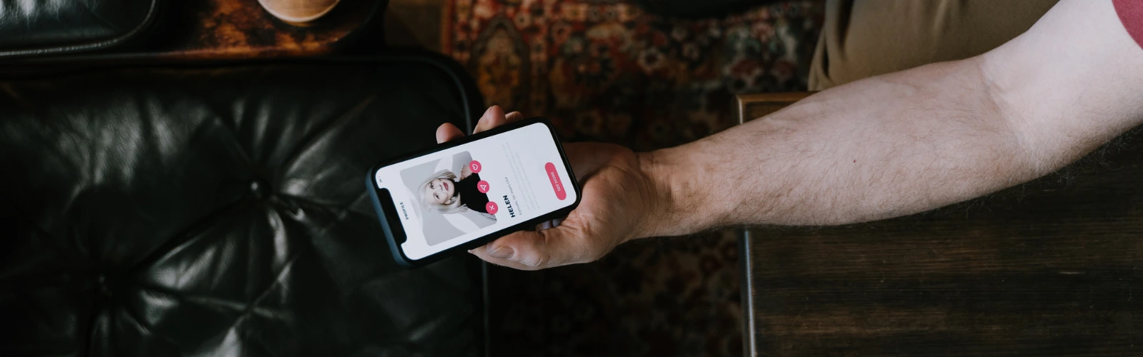 Nahaufnahme einer Hand, die auf einem Sofa ein Dating-App-Profil auf dem Smartphone betrachtet.