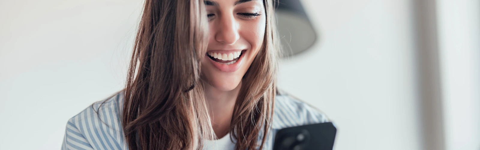 online-flirten-chat-single-frau-lacht Nahaufnahme einer glücklichen Frau, die auf ihr Handy blickt und lacht, wahrscheinlich über eine Chat-Nachricht.