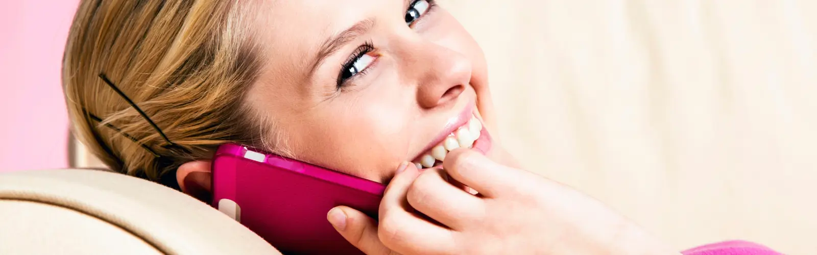 partnersuche-single-frau-telefoniert-date Nahaufnahme einer Single-Frau, die lächelnd auf ihrem rosa Smartphone telefoniert, möglicherweise mit einem Online-Date.